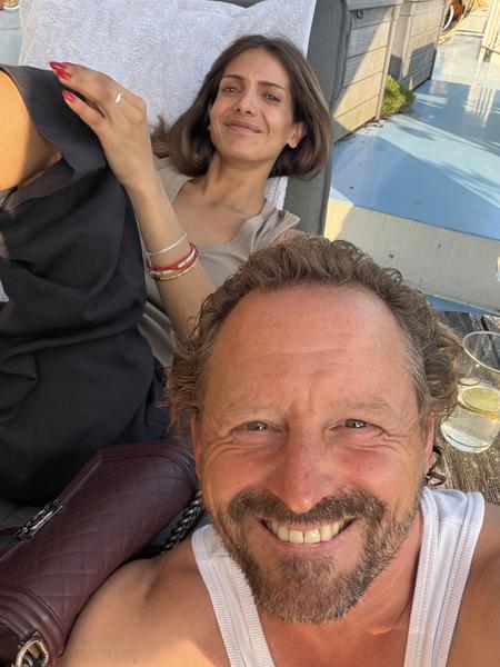 A happy couple is captured in a close-up selfie, relaxing outdoors on what appears to be a sunny deck in Oudeschans, Uilenburg, Amsterdam